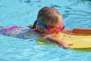 Image is a young girl in goggles learning to swim.