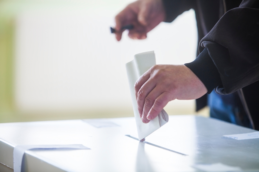 Hand of a person casting a ballot at a polling station during voting.