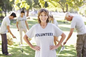 Image is a volunteer Group Clearing Litter In Park Wearing Voulnteer T Shirts and Smiling