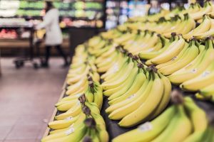 Image is a close up bananas with grocery store patron in the background
