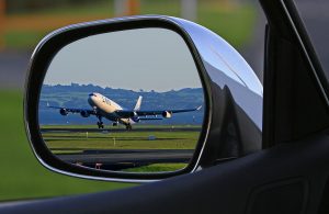 Image is of a jet liner taking off reflecting in a vehicle's side mirror.