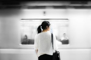 Image is of a girl standing in front of a moving subway car.