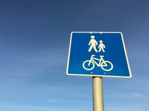 Image is a pedestrian and cycling road sign against a blue sky.