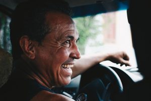 Image is of a smiling man behind the wheel of a car.