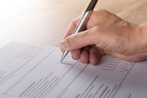 Image is of a person's hand filling out a voting form using a pen.