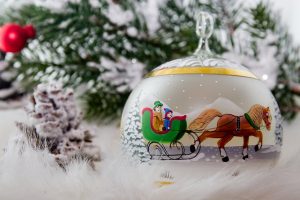 Image is of a Christmas ornament against a backdrop of snow and pine.