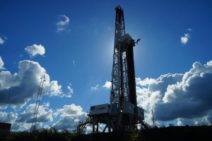 Image is of an oil well drilling platform against a blue sky.