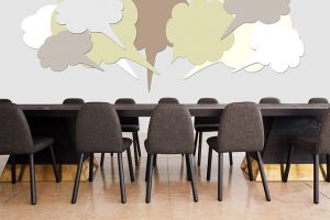 Image is of a conference table and chairs with thought clouds above them.