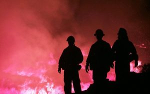 Image is of three firefighters against a wildfire background.