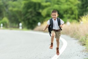 Image is of a small boy skipping down the road with a backpack on.