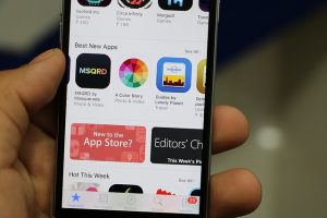 Image is of a hand holding a smartphone open to the App Store.