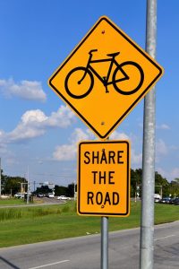 Image is a yellow caution sign with a picture of a bike on it and a "share the road" sign underneath.