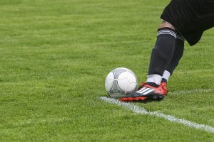 Image is a picture of a soccer player with ball on the green, knees down.