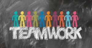 Image is a chalkboard drawn of colorful people on top of the word Teamwork.
