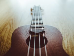 Image is a close up of a ukulele against a wood floor.
