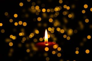 Image is a memorial candle with unfocused pinpoints of lights around it.