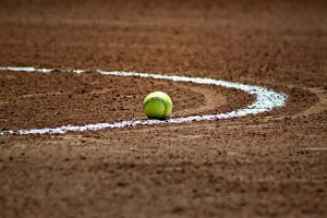 Image is a close up of a softball on a softball infield.  
