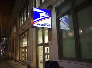 Image is a United States Post Office sign at night.