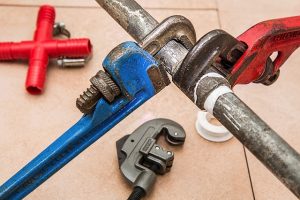 Image is a group of wrenches fixing a plumbing pipe.