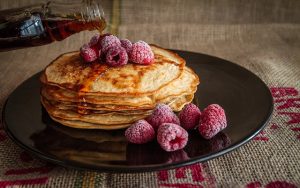 Image is a plate of pancakes with raspberries on top.