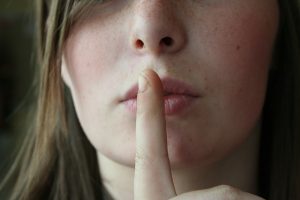 Image is a close up of a woman holding her finger up to her mouth to indicate to be quiet.