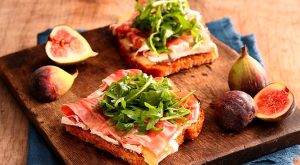 Image is two open faced sandwiches on a board with figs from Kustaa.
