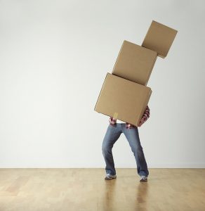 Image is a man standing in an empty room holding a stack of boxes.