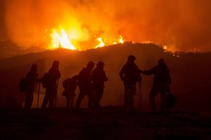 Image is of firefighters silhouetted against a hill on fire.