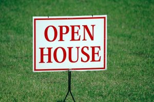 Image is a open house sign on a green lawn.