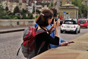 Image is of two girls touring a city, taking pictures.