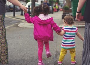 Image is two small children walking hand-in-hand with two adults on a street.