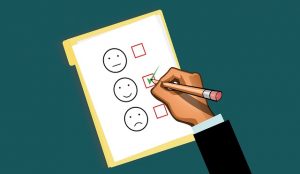 Image is an illustration of a survey with a hand checking the smiley face option rather than the neutral and sad faces.