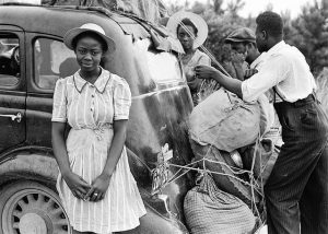 Image is a historical picture of an African American family packing up a car, likely in the 40s or 50s.