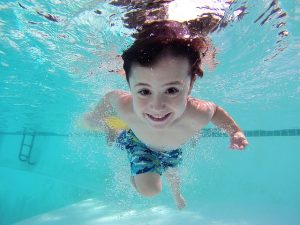 Image is a young boy swimming underwater in a pool.