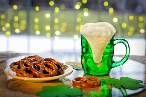Image is of a plate of pretzels and a green beer with shamrocks in the foreground.