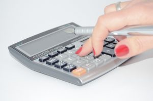 Image is a woman's hand holding a fountain pen while using a calculator.