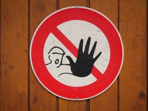Image is a round sign on a wooden wall that has a red circle with a line across it showing a man with a hand out signaling "stop".