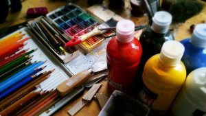 Image is a group of artists paints, colored pencils, and brushes.