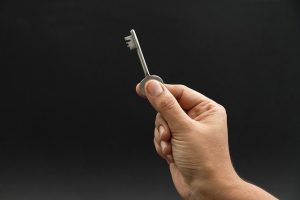 Image is a hand holding a house key against a black background.