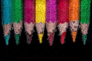 Image is a group of colored pencils in liquid against a black background, with air bubbles clinging to the pencils.
