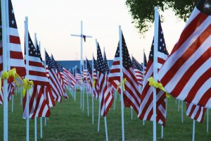 Image is a field of American Flags with yellow ribbons tied on each flag pole.