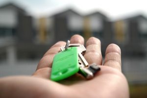 Image is a close up of a hand holding property keys with townhouses in the background.