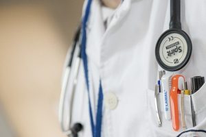 Image is the close up of a doctor's coat with stethoscope around the neck and pens in pocket.