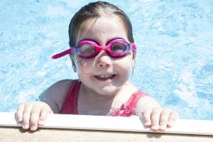Image is a little girl in a pool with swim goggles.  