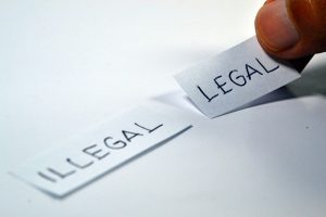 Image is a close up of someone putting a paper with the word legal next to a paper with the word illegal written on it.