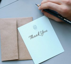 Image is someone writing a thank you note.
