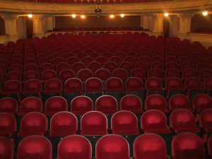 Image is of empty theater seats in an auditorium.