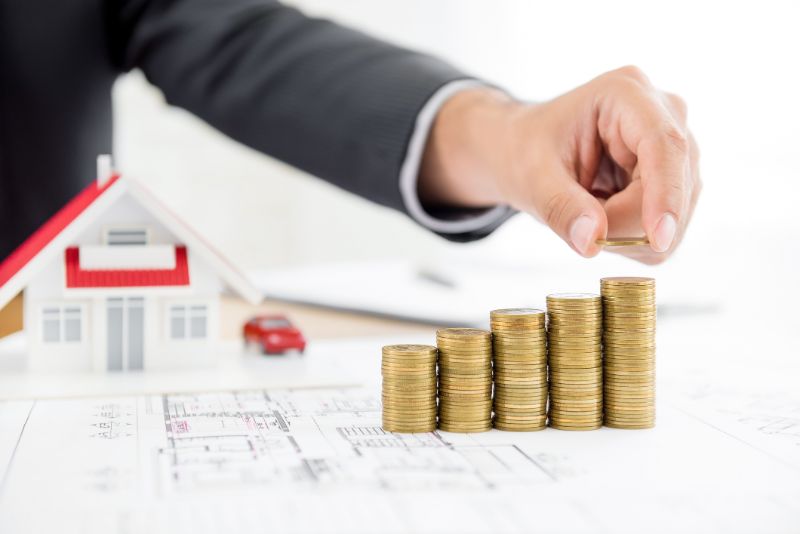 businessman putting coin on top of money stacks with blurred house